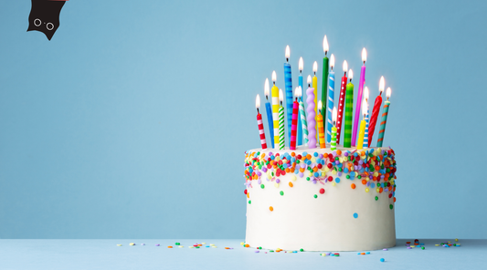birthday cake with candles on blue background with black cat peeking out of the corner